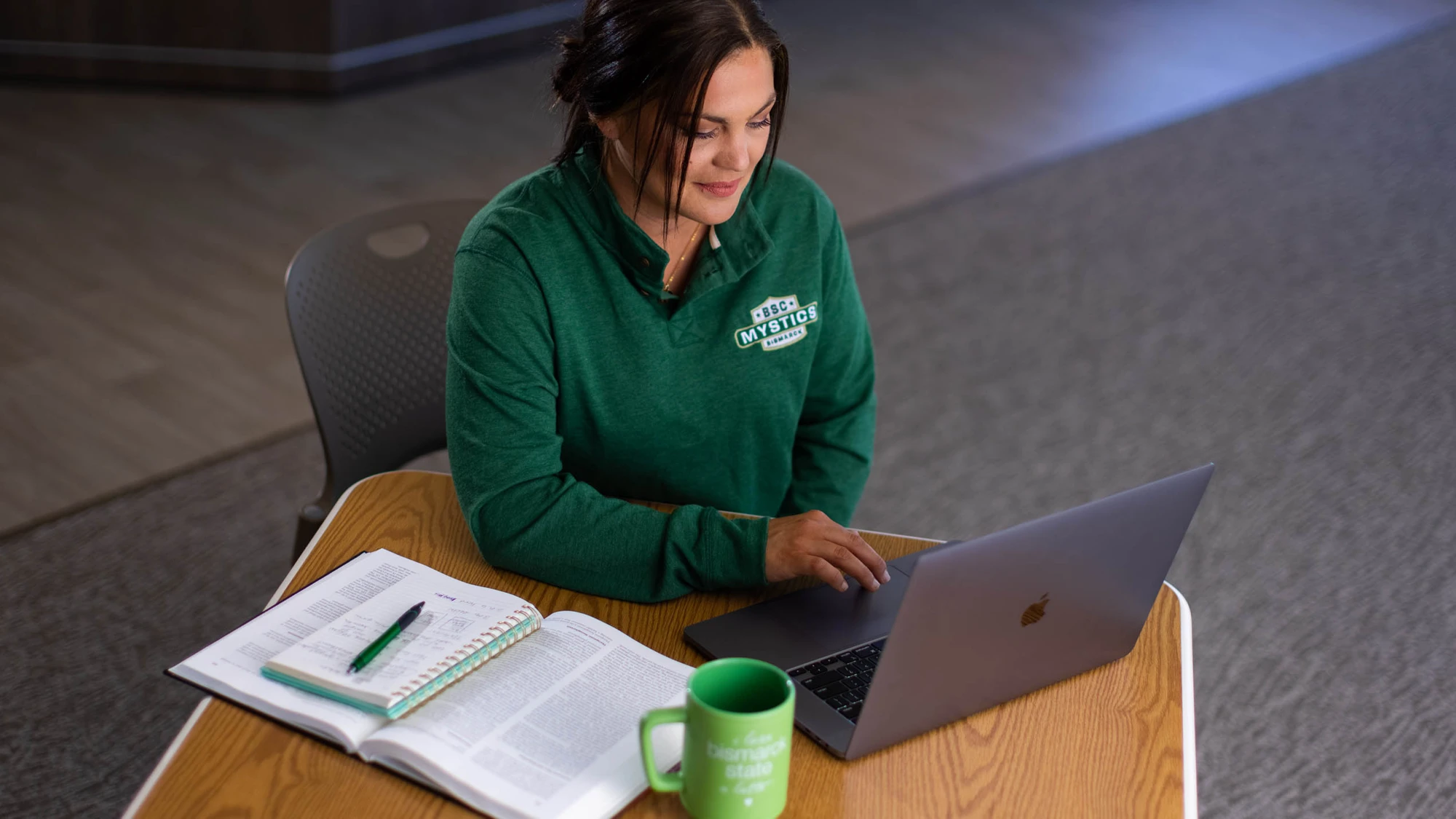 adult student working online at computer in a green sweatshirt