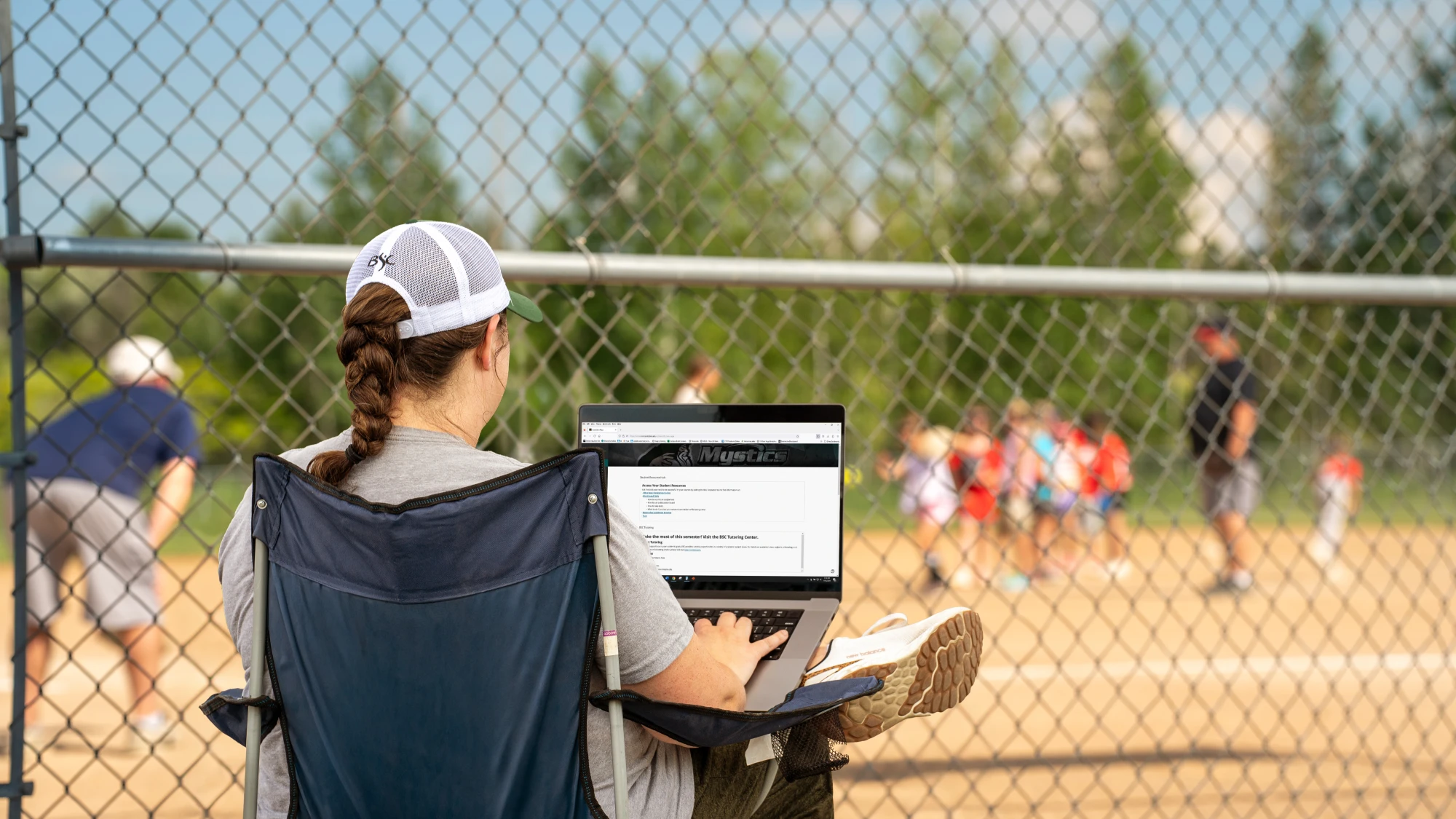 mom with braid on laptop watching kids softball practices
