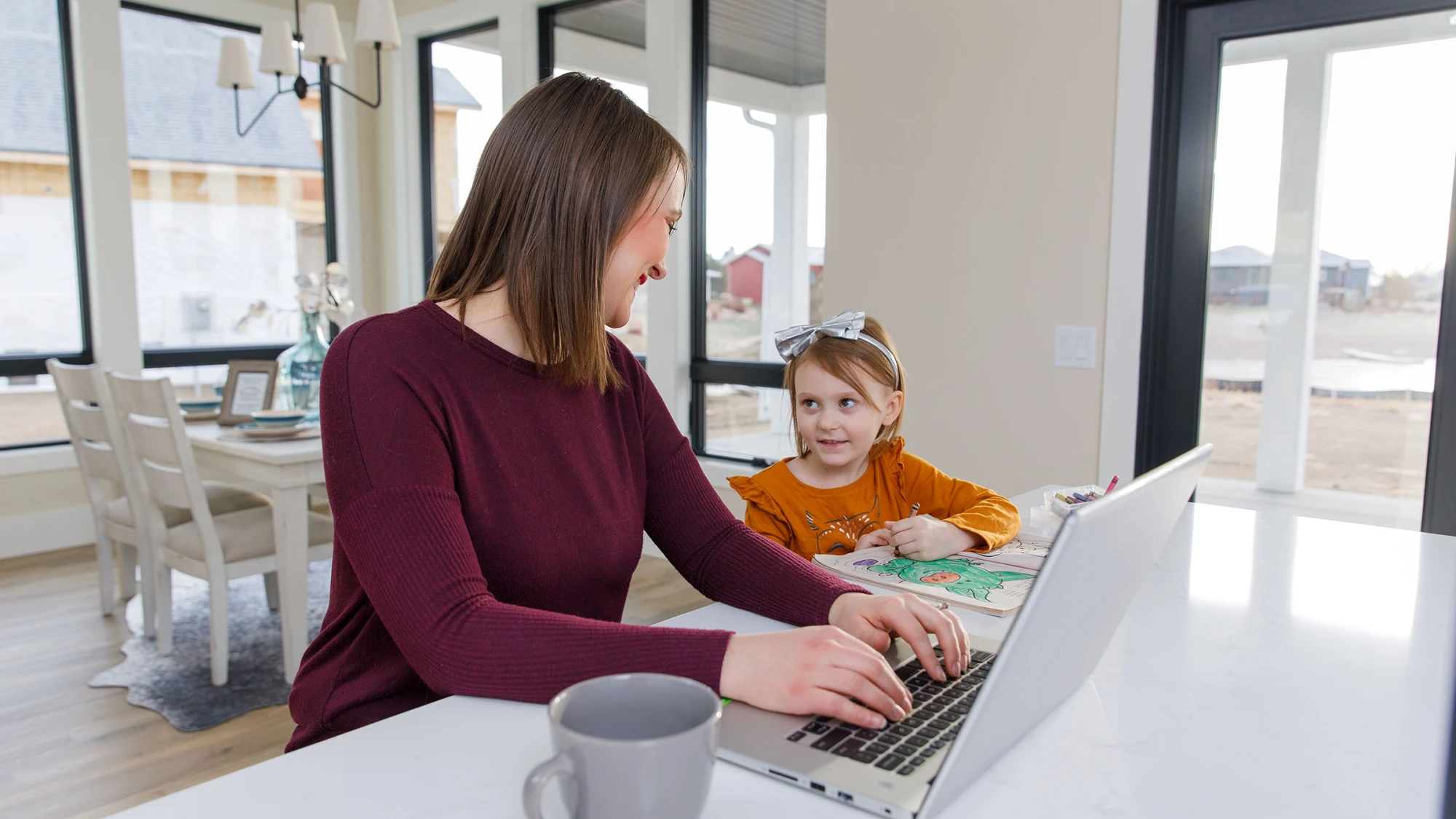 mom working on computer in kitchen at island with daughter coloring