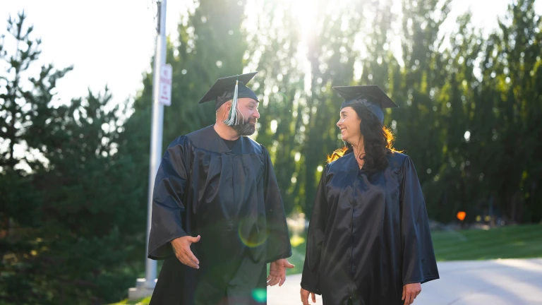 two adult graduates from Bismarck State College in cap and gowns